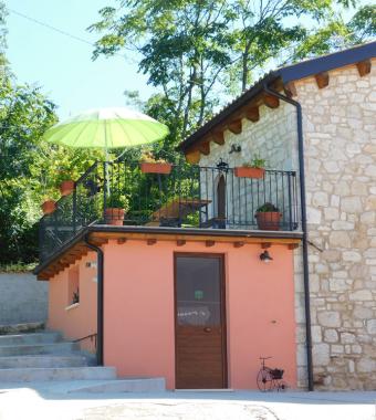 Casa di pietra con terrazza, ombrellone verde e fioriere.