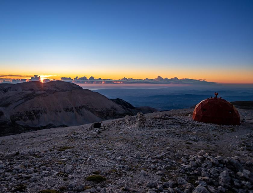 Tramonto montano con rifugio geodetico e paesaggio roccioso.