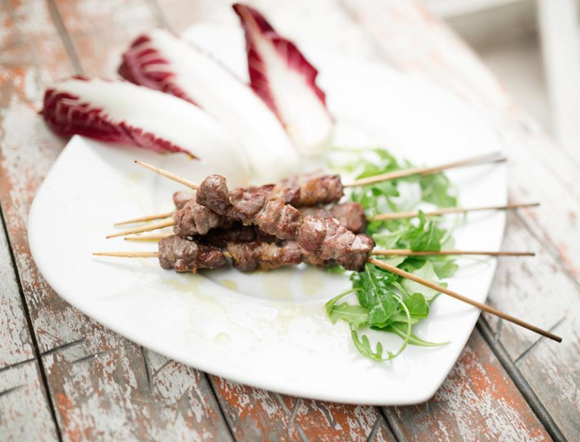 Spiedini di carne con rucola e radicchio su piatto bianco.