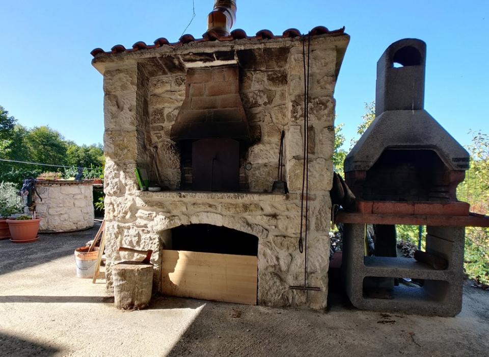 Forno a legna in pietra con barbecue accanto, in ambiente esterno.